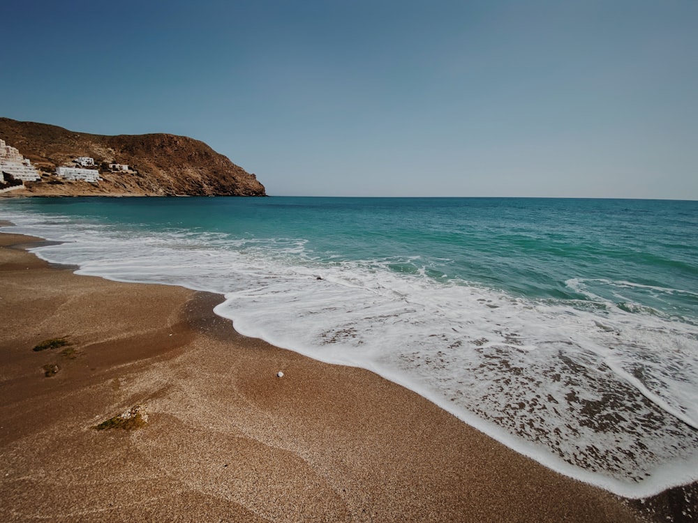 Plage de sable brun avec de l’eau bleue de l’océan pendant la journée