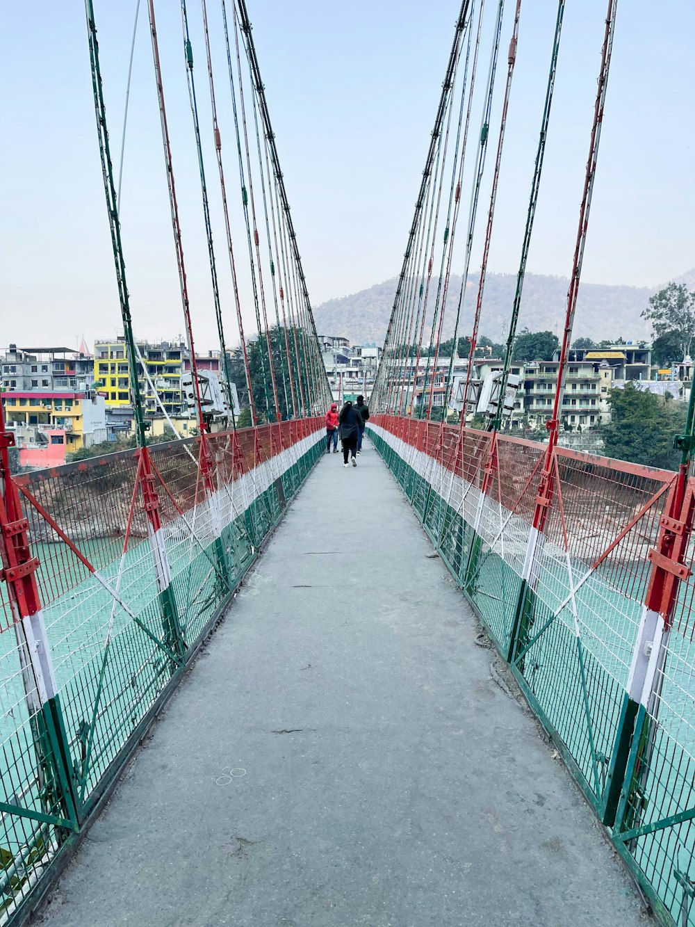 昼間、赤い金属製の橋の上を歩く黒いジャケットを着た人物