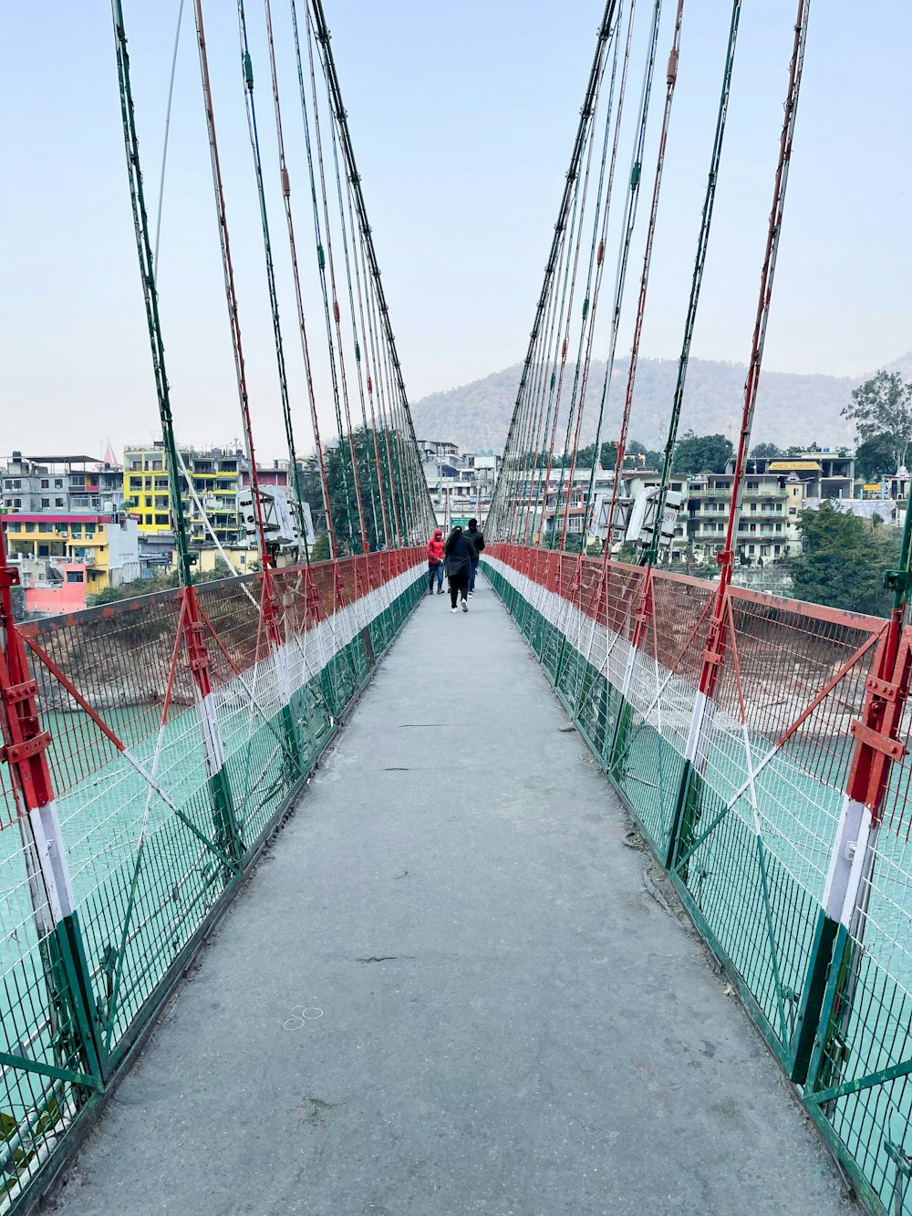 Person in schwarzer Jacke geht tagsüber auf der roten Metallbrücke