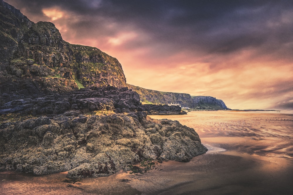 brown and green rock formation on beach during sunset