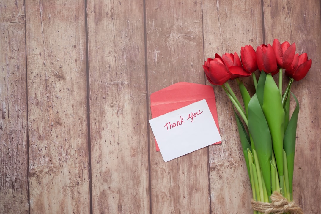 red tulips on white printer paper, thank you message, envelope and red tulip flower on wooden background.