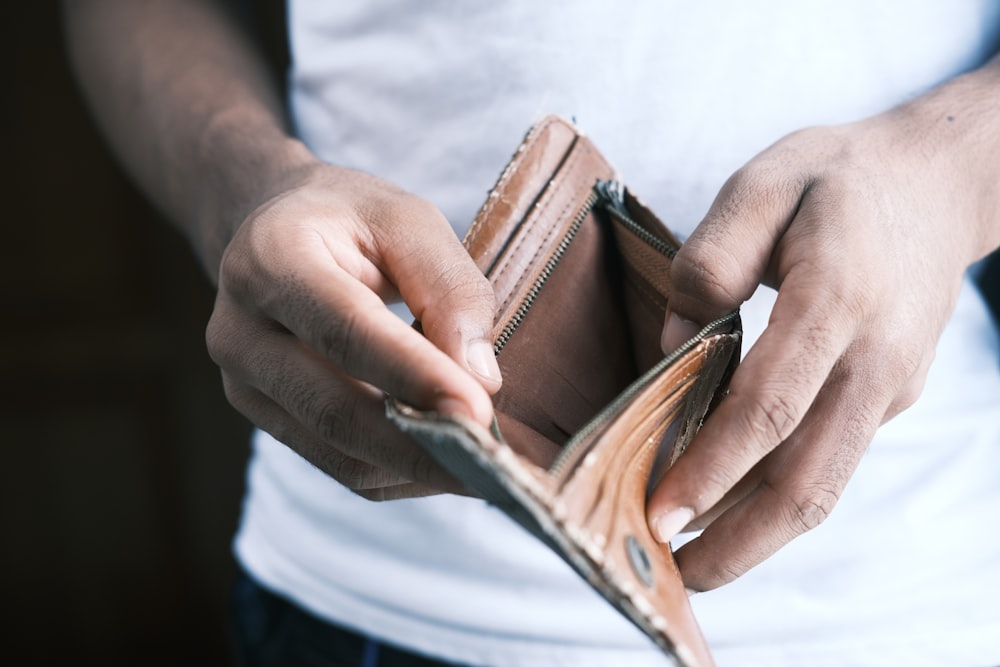 personne tenant un portefeuille à deux volets en cuir marron