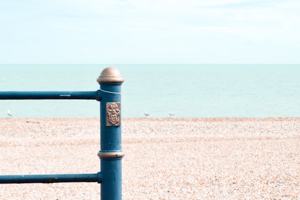 valla de metal azul en arena marrón cerca del mar durante el día