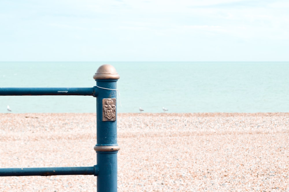 blue metal fence on brown sand near sea during daytime