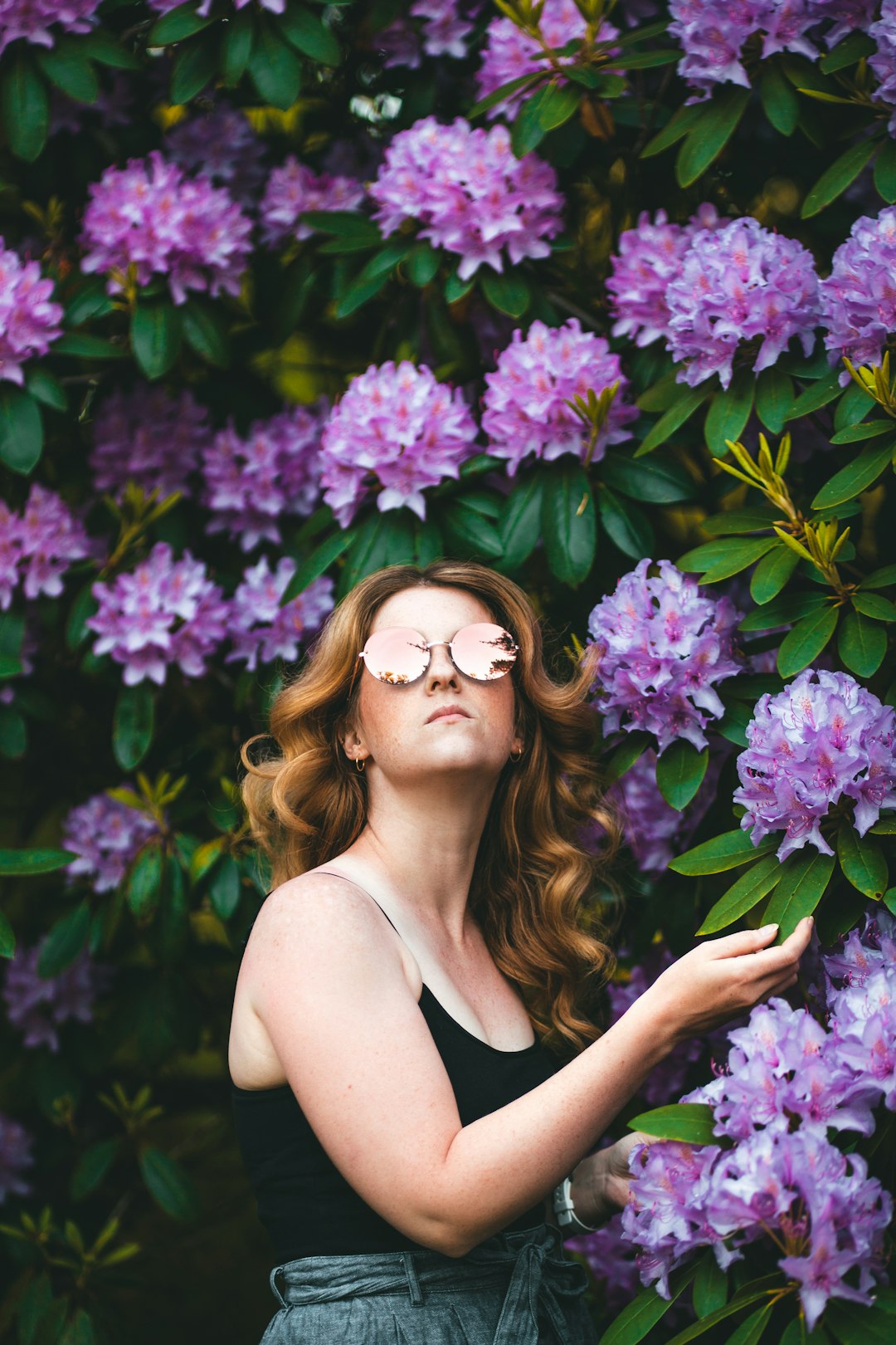 woman in black tank top wearing eyeglasses standing beside purple flowers