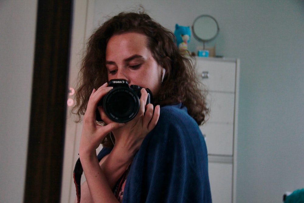 woman in blue robe holding black nikon dslr camera