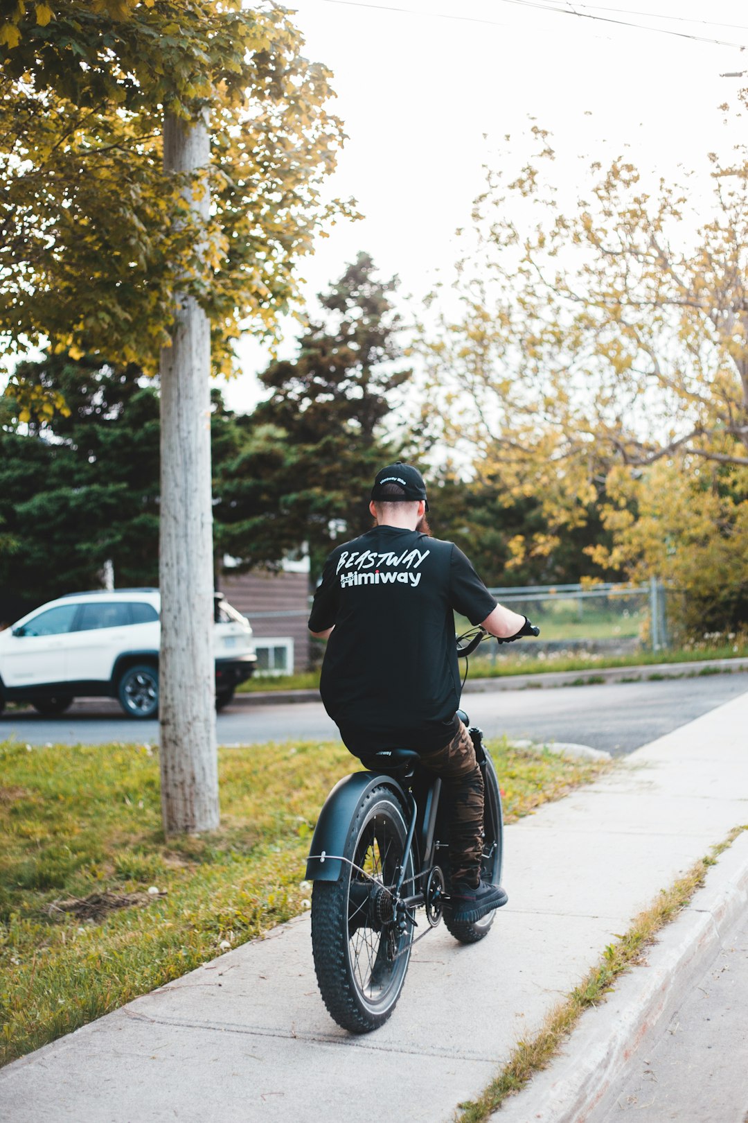 man in black and white adidas t-shirt riding bicycle on road during daytime