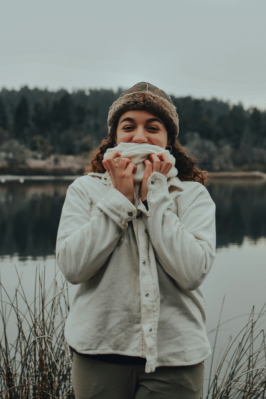 woman in white coat holding white ceramic mug near body of water during daytime