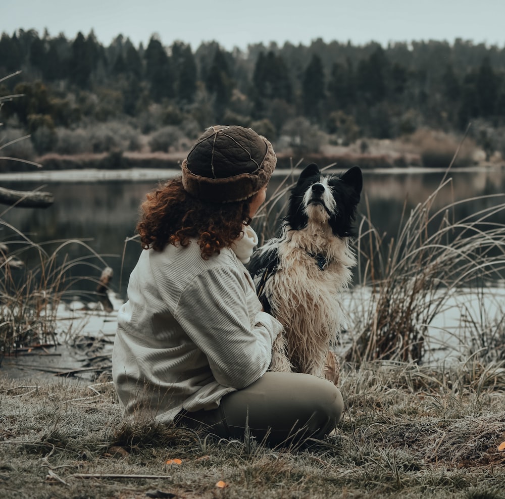 woman in beige jacket sitting beside black and white dog