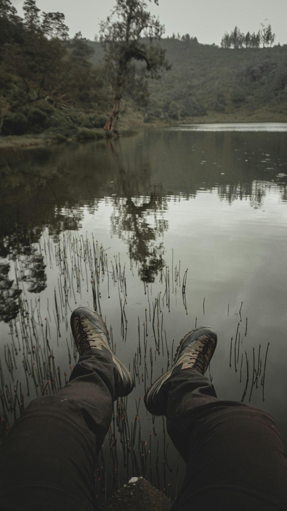 person in brown pants and black shoes sitting on rock near lake during daytime