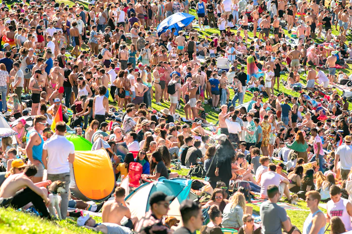 A lively crowd enjoying a sunny outdoor stage with colorful banners and people playing lawn games.