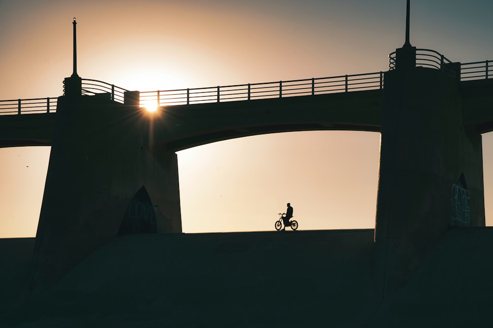 silhouette of 2 people standing on concrete bridge during sunset