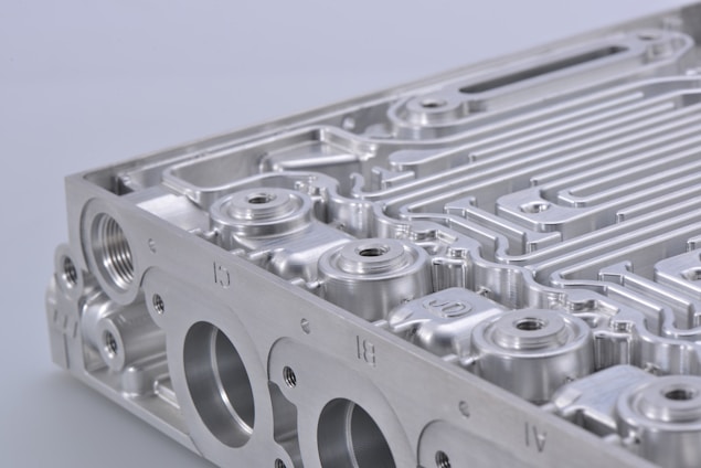 A close-up view of a metallic component, featuring intricate grooves and perfectly machined surfaces. The object appears to be part of an industrial or mechanical structure with multiple circular openings and linear patterns.