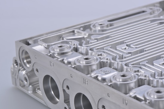 A close-up view of a metallic component, featuring intricate grooves and perfectly machined surfaces. The object appears to be part of an industrial or mechanical structure with multiple circular openings and linear patterns.