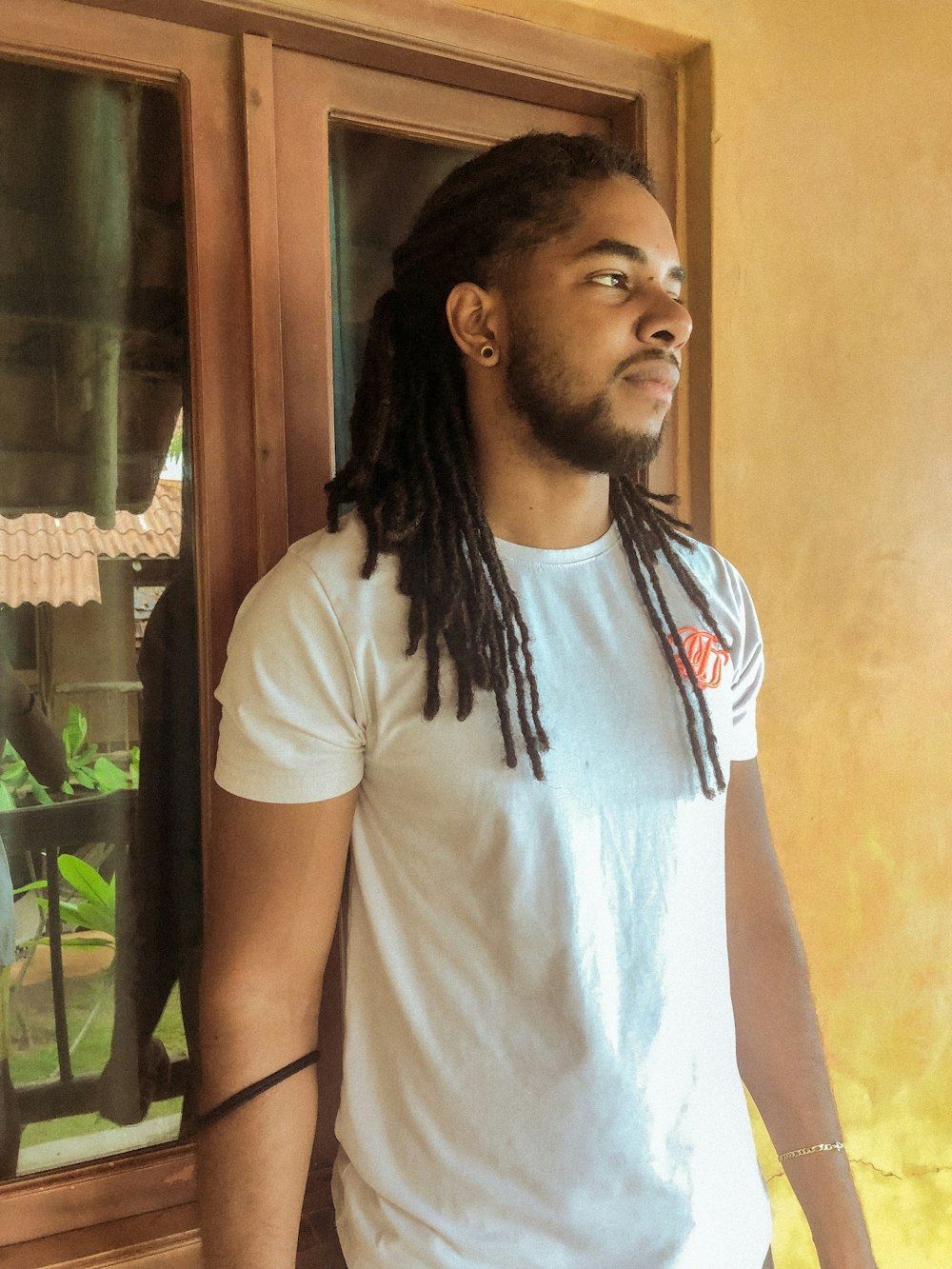 man in white crew neck t-shirt standing near brown wooden door