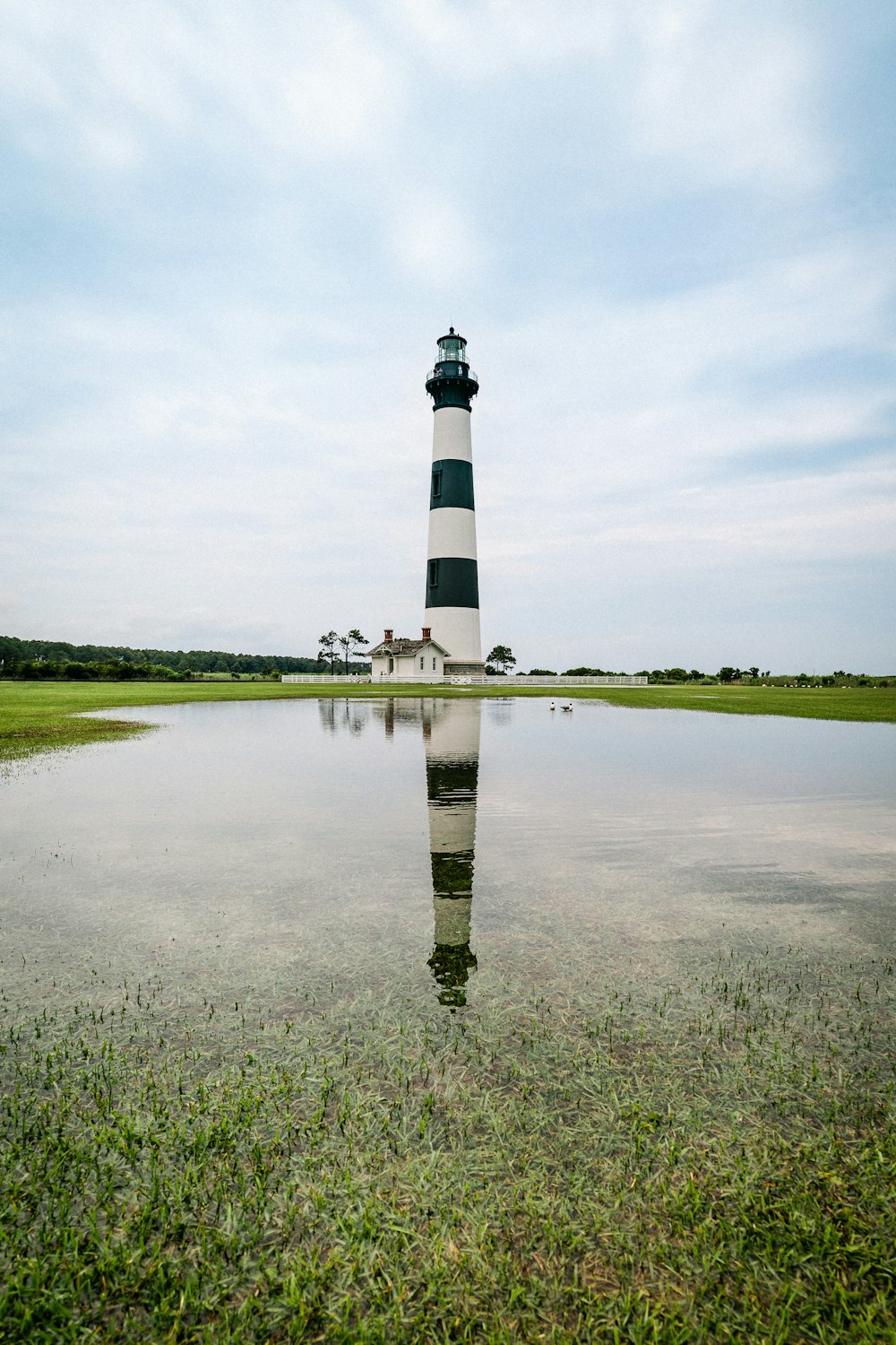 black and white lighthouse near green grass field under white clouds during daytime