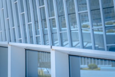 Glass panels and metallic structures form the facade of a modern architectural building. The reflection on the windows suggests minimalistic urban design with linear and geometric patterns.