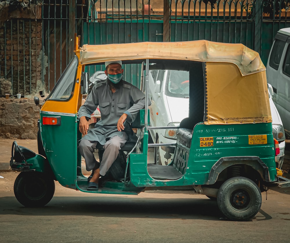 Hombre en chaqueta de mezclilla azul sentado en rickshaw automático verde y amarillo