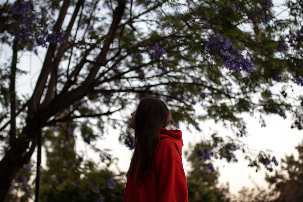 woman in red hoodie standing under green tree during daytime