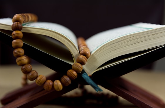 A close-up image of a traditional wooden tesbih (prayer beads) resting on an open Quran.