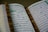 An open book with Arabic script is displayed, likely a religious text. A string of brown prayer beads is placed across the pages.
