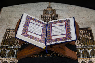 An open Quran with elegant Arabic calligraphy on a wooden stand.