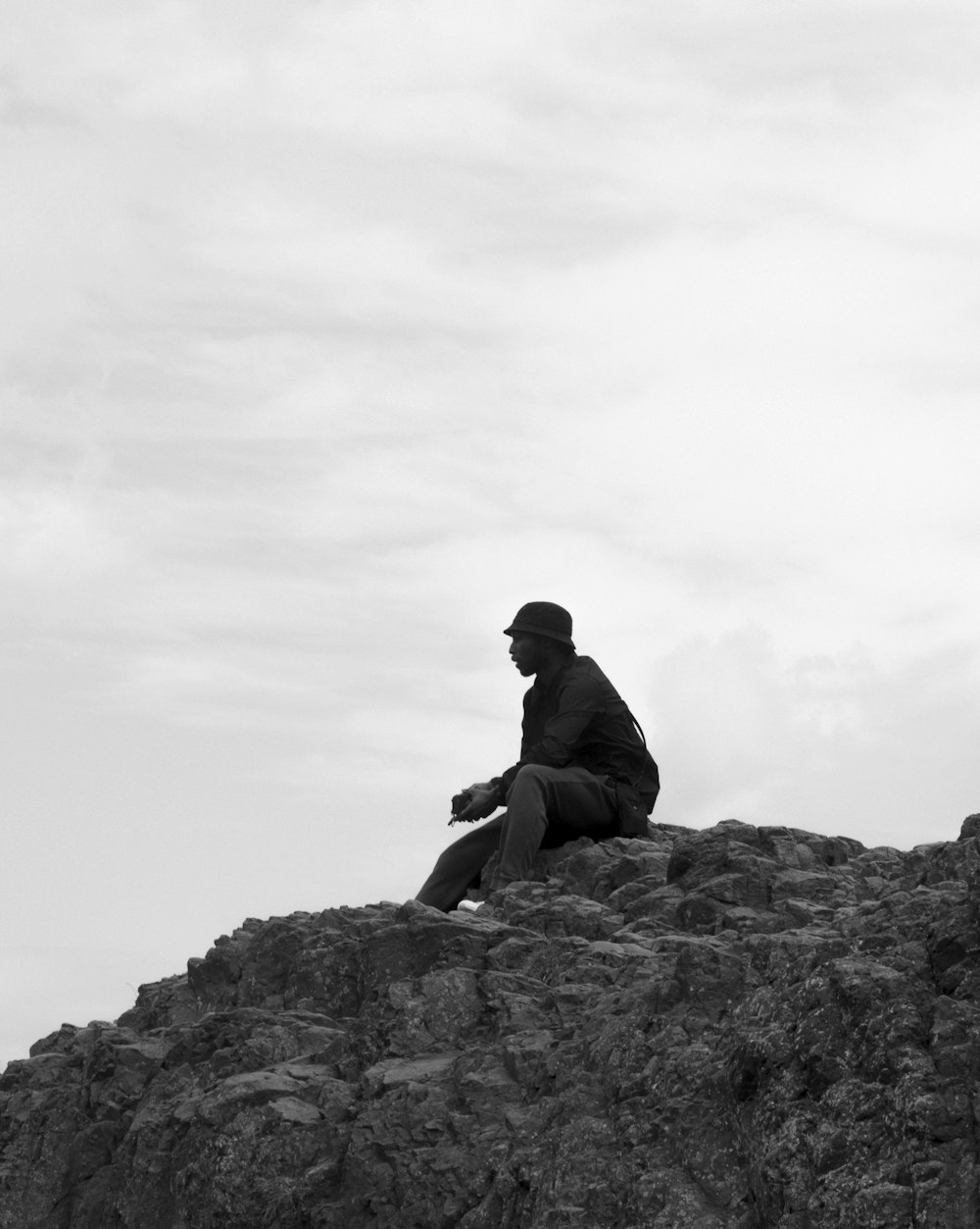 grayscale photo of man sitting on rock