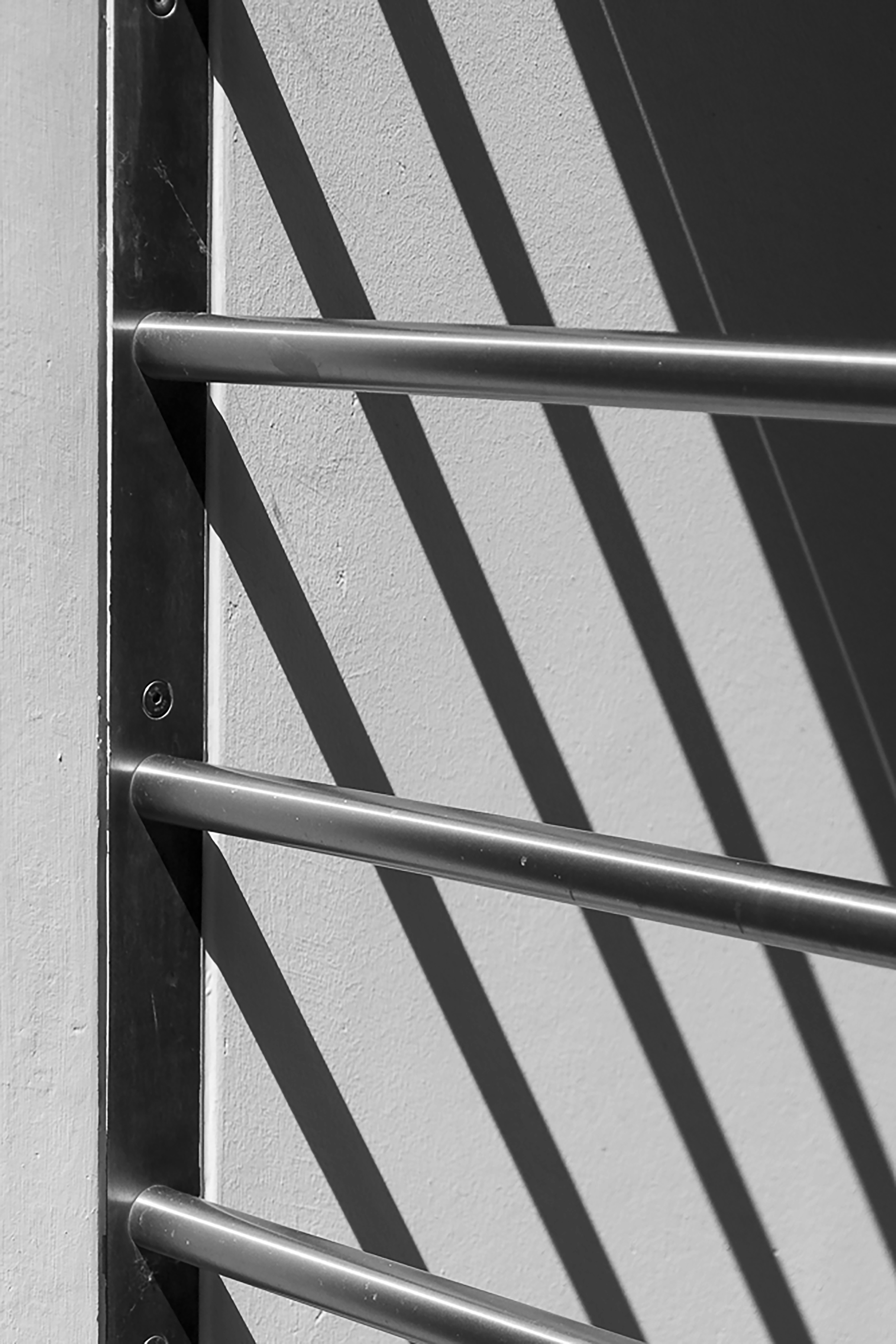 Close-up of ornate black metal grille on white wall, sharp detail, deep shadows on metal bars