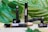 A variety of brown glass vials labeled 'Scentl.' are placed on a wooden surface surrounded by large green tropical leaves. Some vials are lying down, while others stand upright, and one appears to have an open cap.