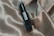 A small, dark glass bottle labeled 'Scentil' lies diagonally against a backdrop of smooth, beige satin fabric with flowing textures and soft folds. The label on the bottle is clear and elegant, adding a touch of luxury to the overall composition.
