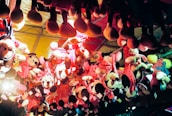 Several plush toys, mostly of a popular cartoon character, hang upside down from the ceiling as part of a carnival or amusement park prize display. The toys are predominantly dressed in red and pink polka-dotted outfits and have large round ears. The lighting gives the scene a warm, colorful glow, enhancing the festive atmosphere.