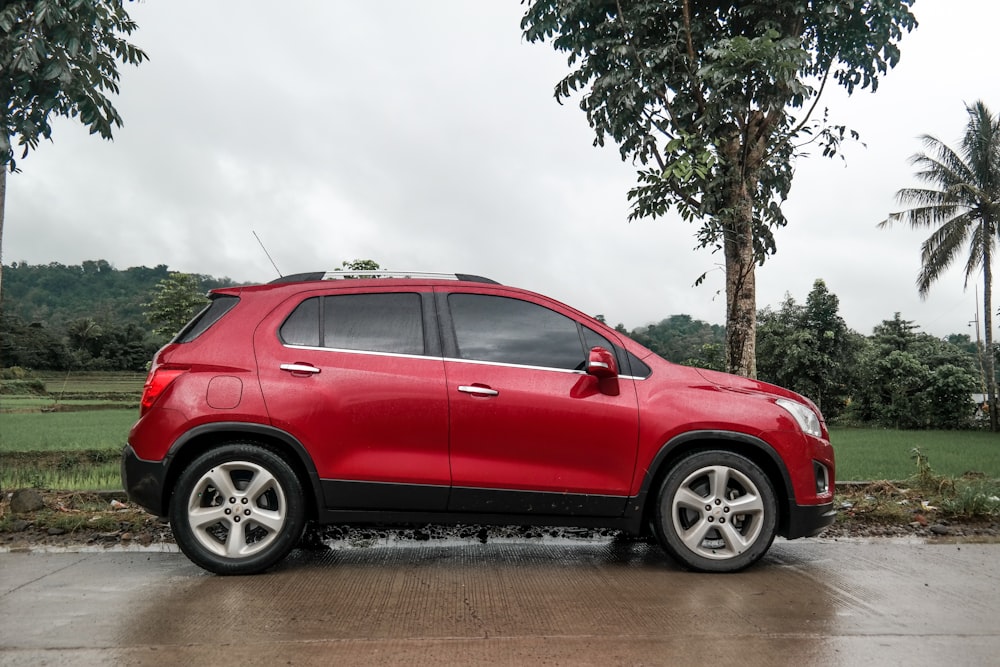 red 5 door hatchback parked beside green tree during daytime