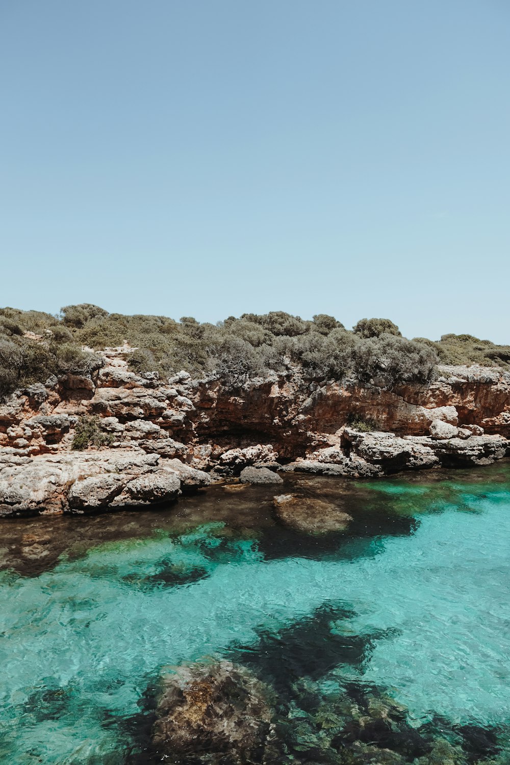 brown rocky mountain beside blue sea under blue sky during daytime