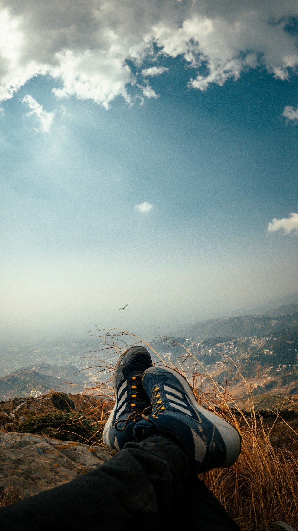 person in black and white adidas sneakers sitting on brown rock formation during daytime