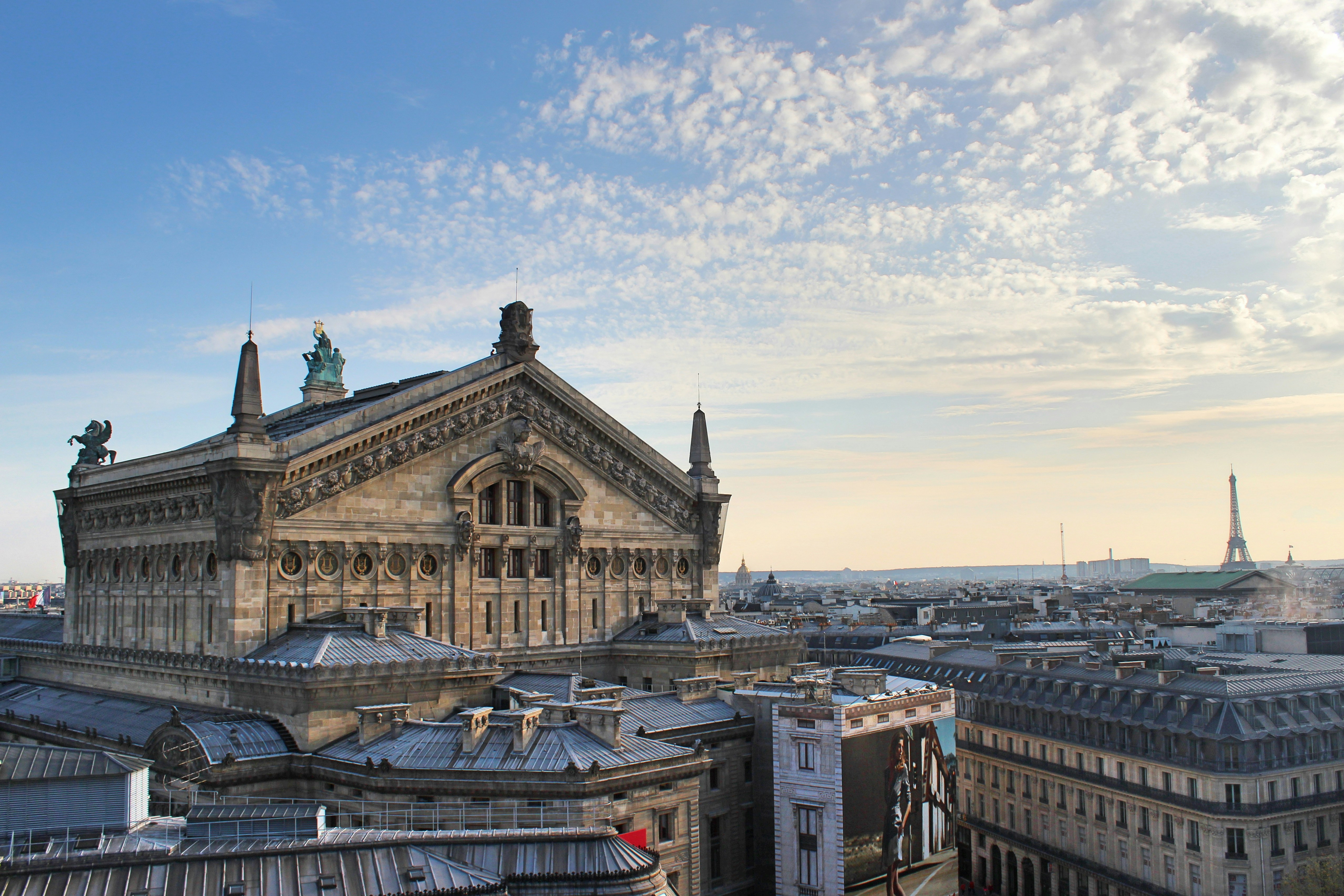 brown and gray concrete building under blue sky during daytime, Back of the Palais Garnier opera house seen from the roof of Galeries Lafayette in Paris, France.
