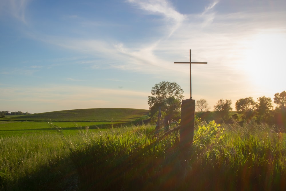 cruz cinzenta no campo verde da grama sob o céu azul durante o dia