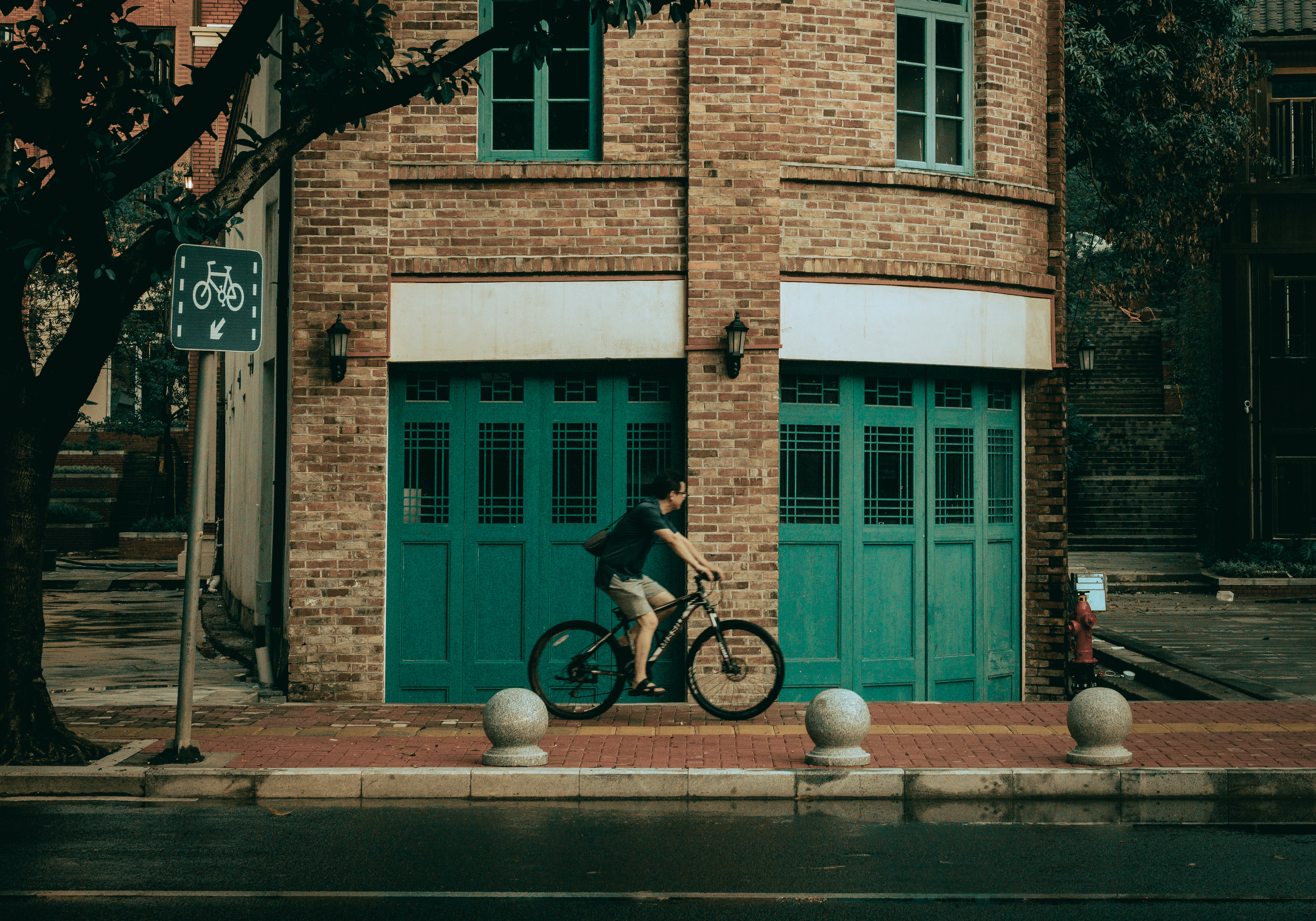 man in blue shirt and black pants riding on bicycle near brown brick building during daytime