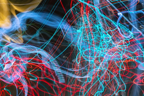 A vibrant display of chaotic light patterns with intertwining arcs and loops, primarily in shades of blue, red, and yellow. The lines flow dynamically across a dark background, creating an energetic and abstract visual.