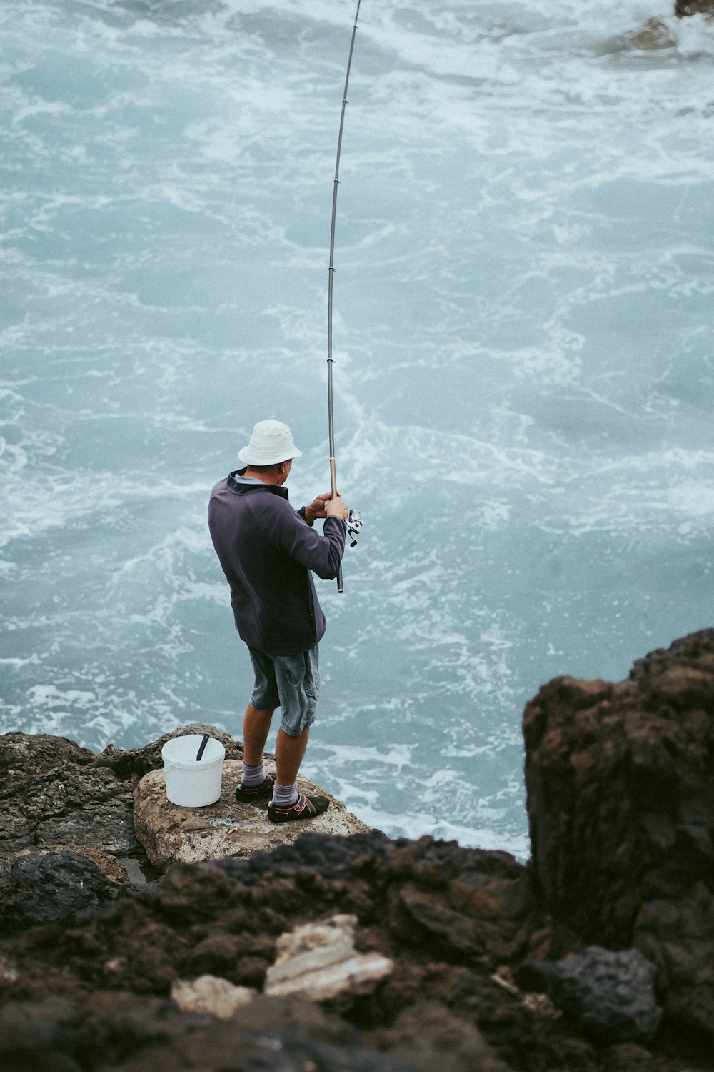 man in black jacket fishing on sea during daytime