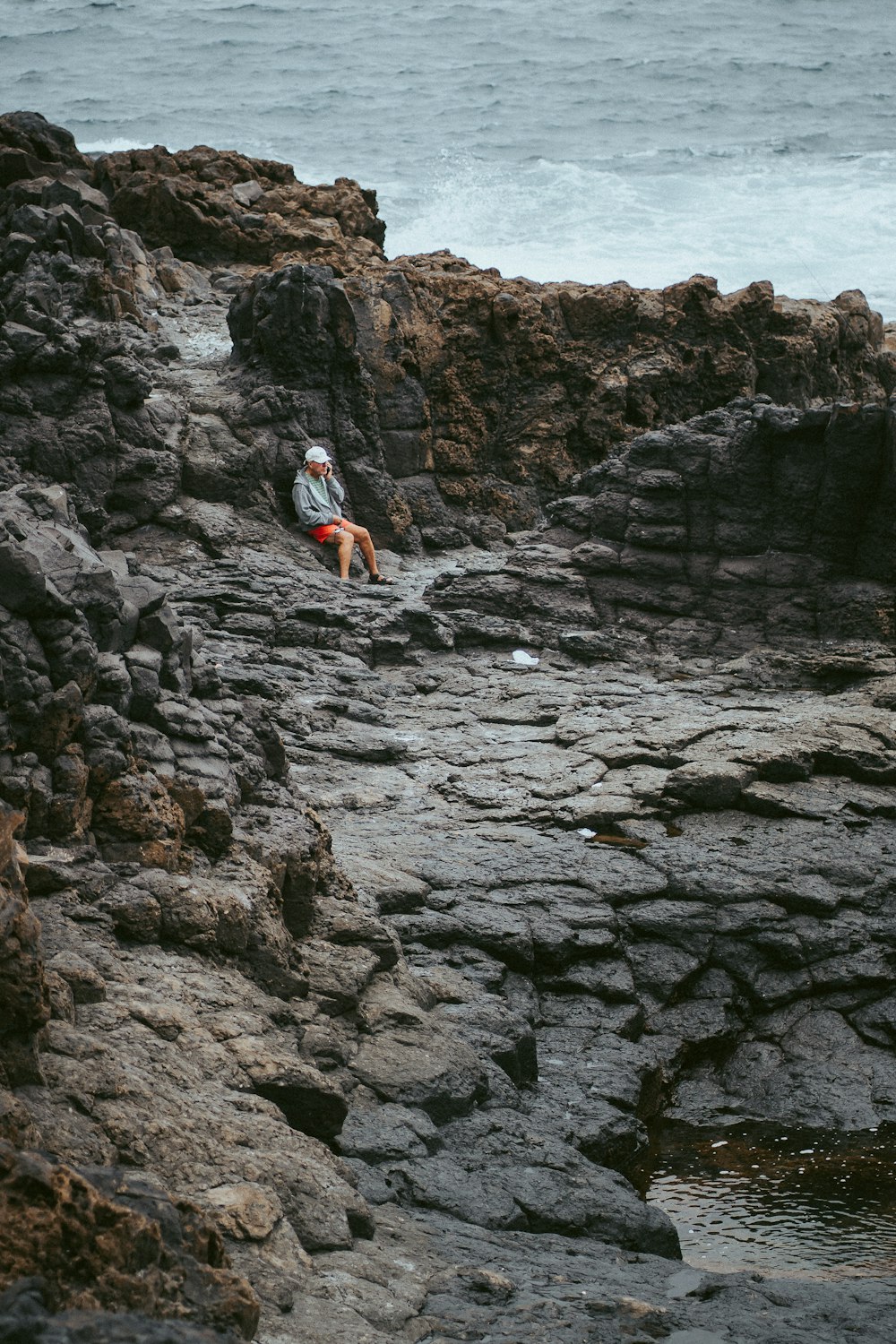 person in white shirt and blue denim shorts sitting on rocky mountain during daytime