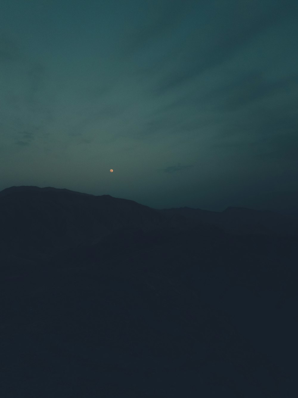 silhouette of mountains under blue sky with moon