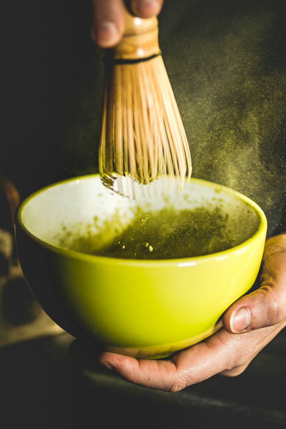 person holding yellow ceramic bowl with green soup