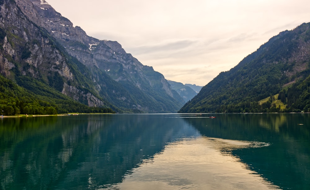 lake near mountain under white sky during daytime