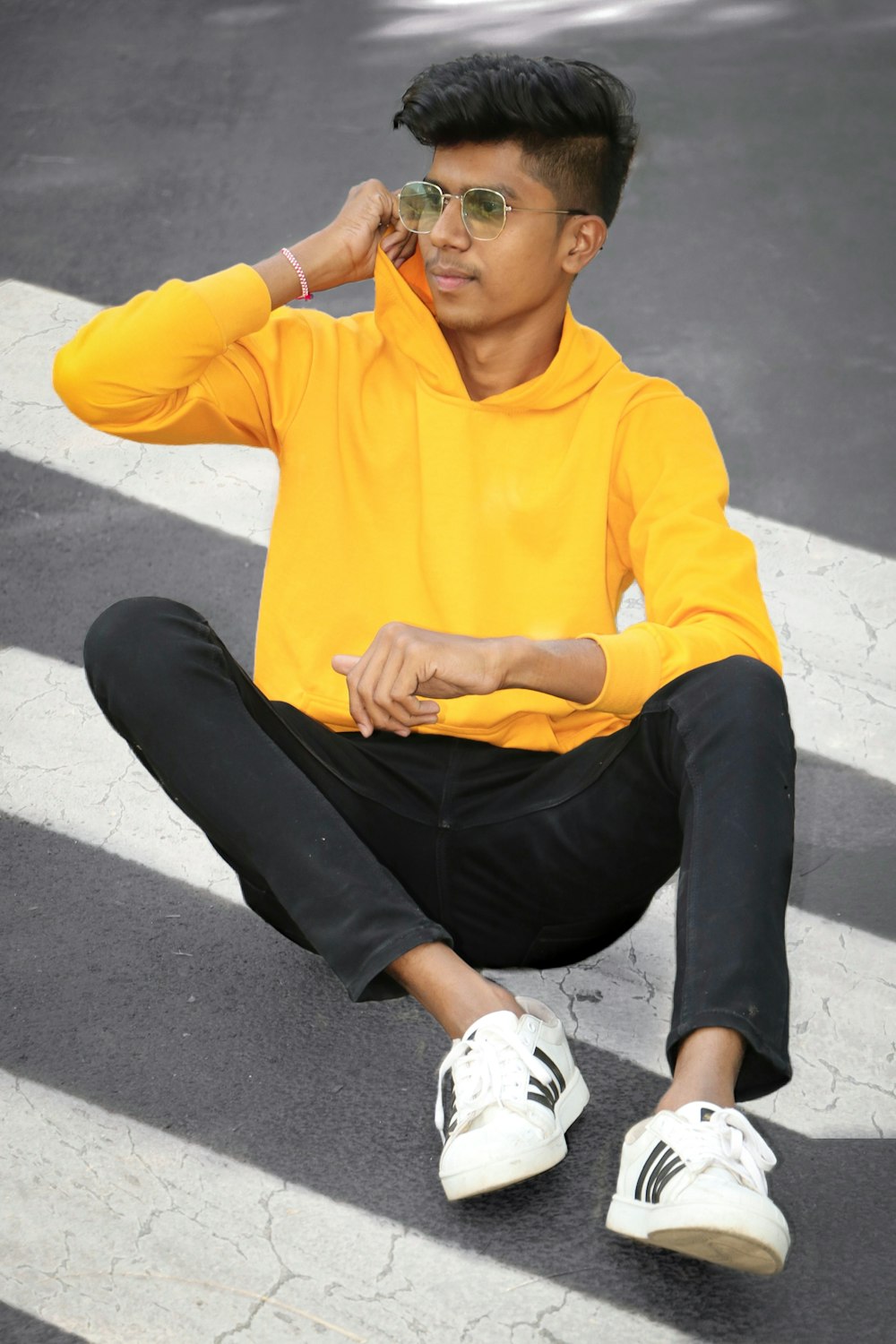 man in yellow hoodie and black pants sitting on gray concrete floor