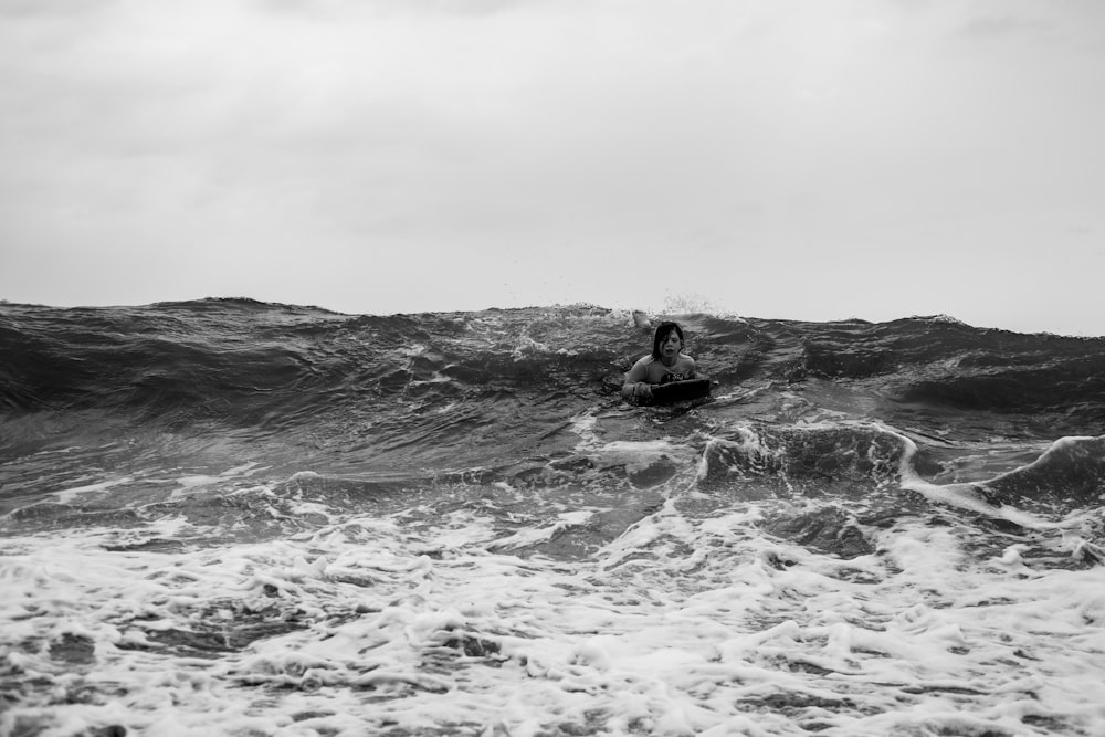 grayscale photo of man surfing on sea waves