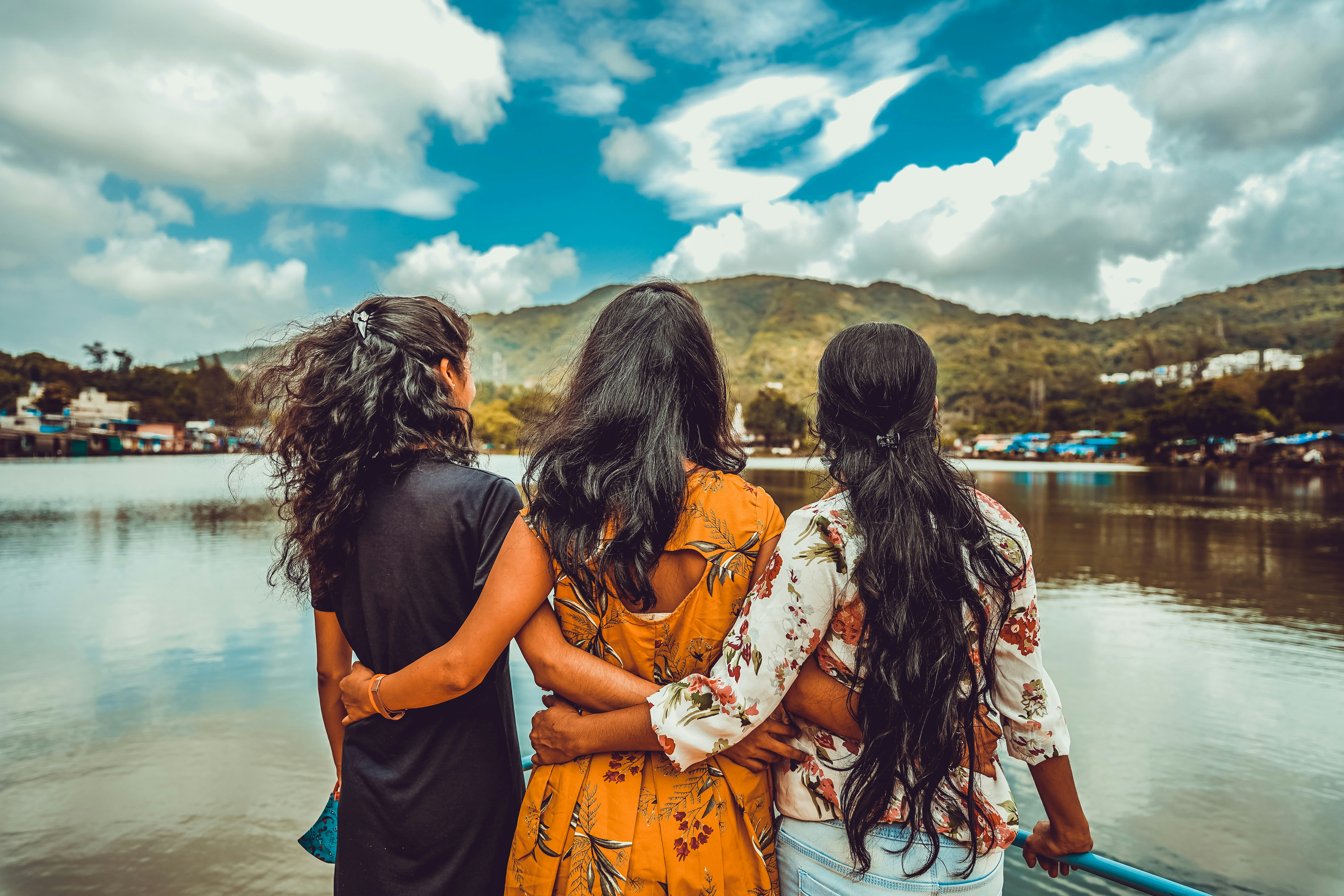 2 women in black and orange floral dress standing near body of water during daytime