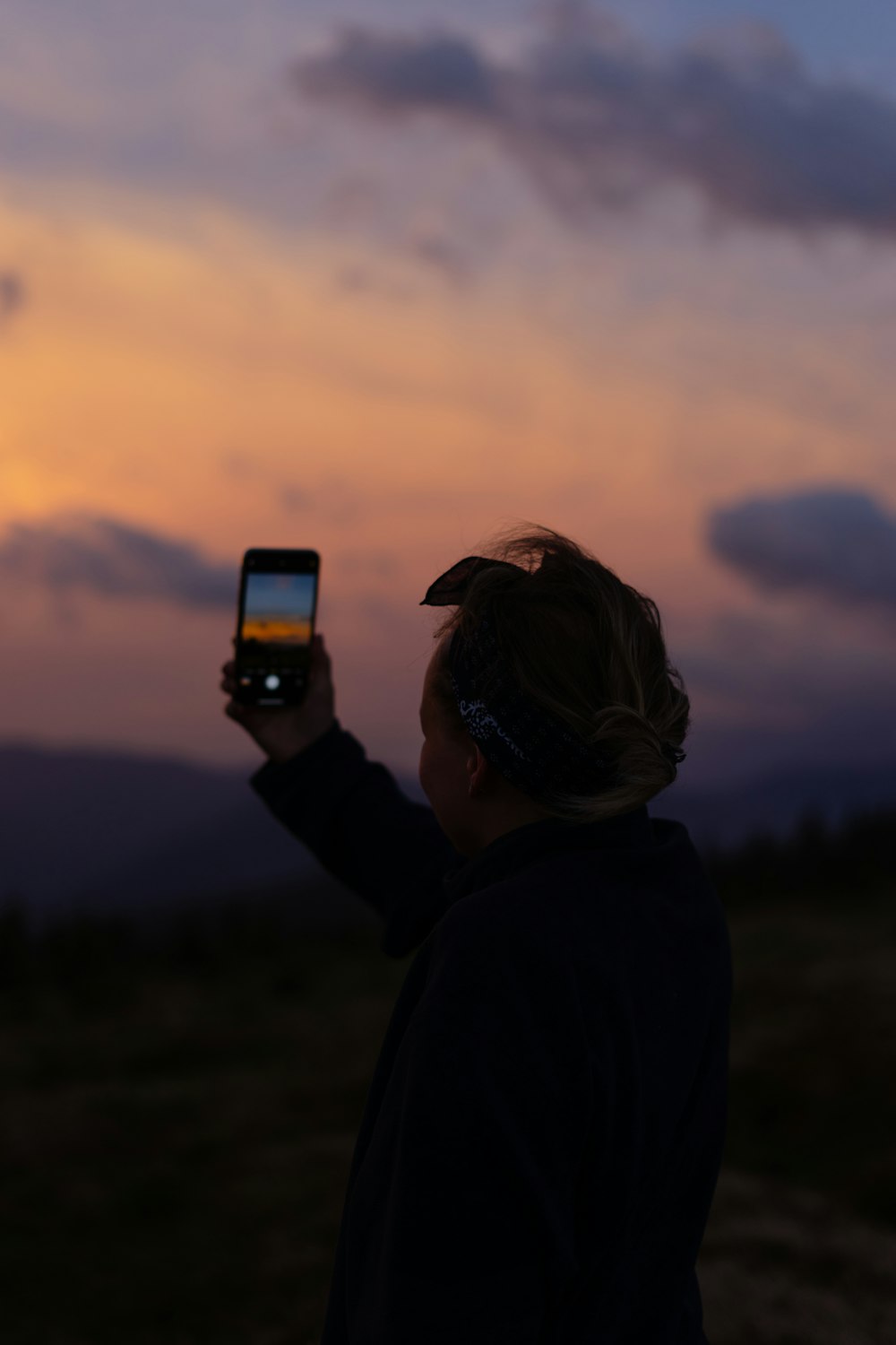 person holding smartphone taking photo of sunset