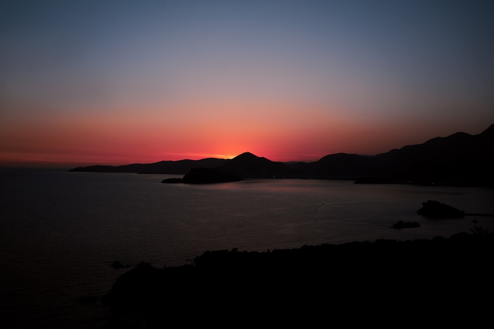 silhouette of mountain near body of water during sunset