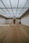 A minimalist interior room with wooden flooring and a large, geometric triangular structure as the centerpiece. The ceiling is made of glass panels that diffuse soft light throughout the space, creating a serene ambiance. The walls are plain and complement the simplicity of the design.