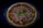 A freshly baked pizza topped with sliced red onions, grated cheese, and garnished with a fresh basil leaf at the center. The crust is golden brown, and the pizza is placed in a round baking dish against a dark background.